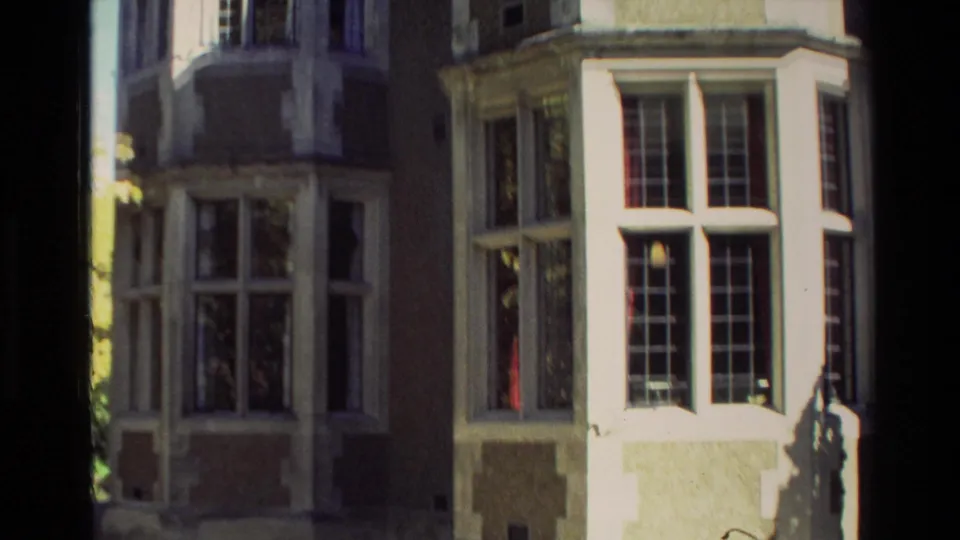 1982 New Zealand 8mm frame showing lower sections of the mansion facade, including tall bay windows and strong sunlight.