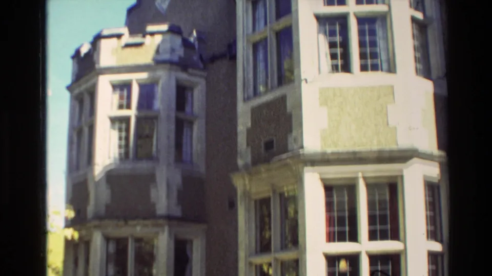 1982 New Zealand home-movie frame showing a sunlit side angle of the Tudor-influenced mansion with multiple bay windows.