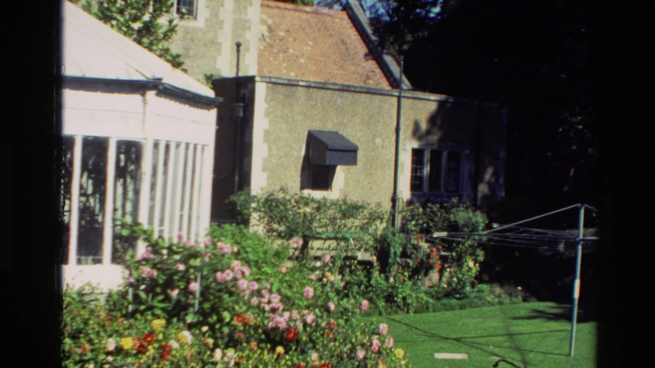 1982 New Zealand 8mm frame showing a residential garden with flowering beds, greenhouse windows, lawn, and a rotary clothesline.