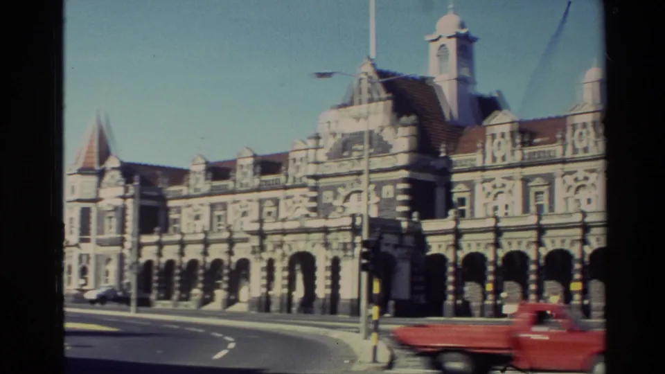 1982 New Zealand 8mm frame showing the landmark's arched stone facade, curved street, traffic island, and passing red vehicle.