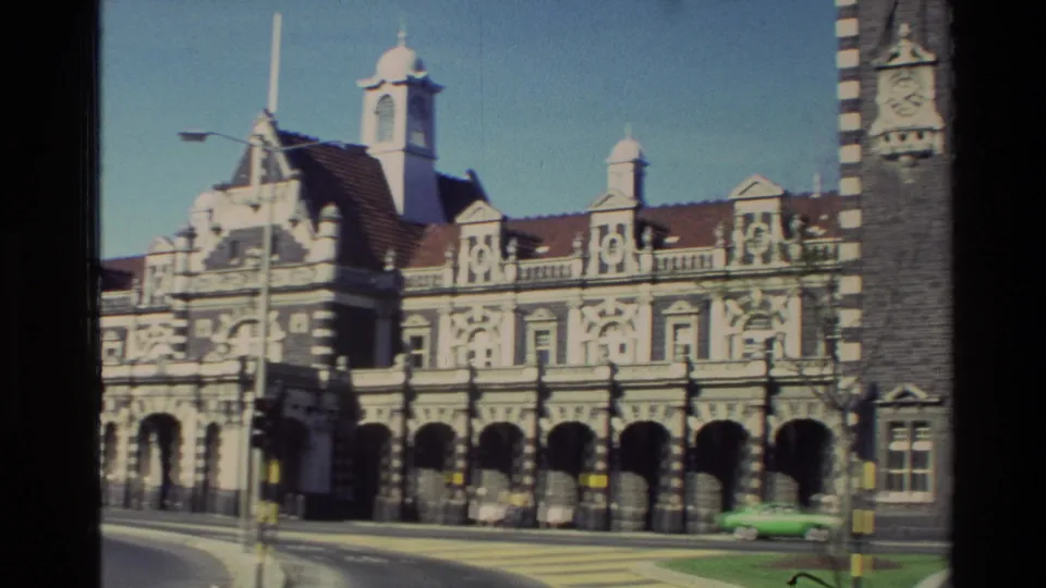 1982 New Zealand frame of the landmark's arched grey stone frontage with road markings, a green car, and part of the clock tower at right.