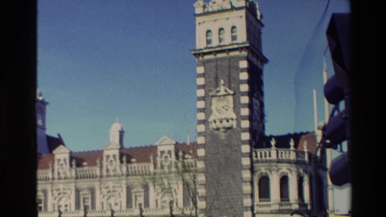 Clock tower and ornate facade seen across a city street with yellow car near the curb.