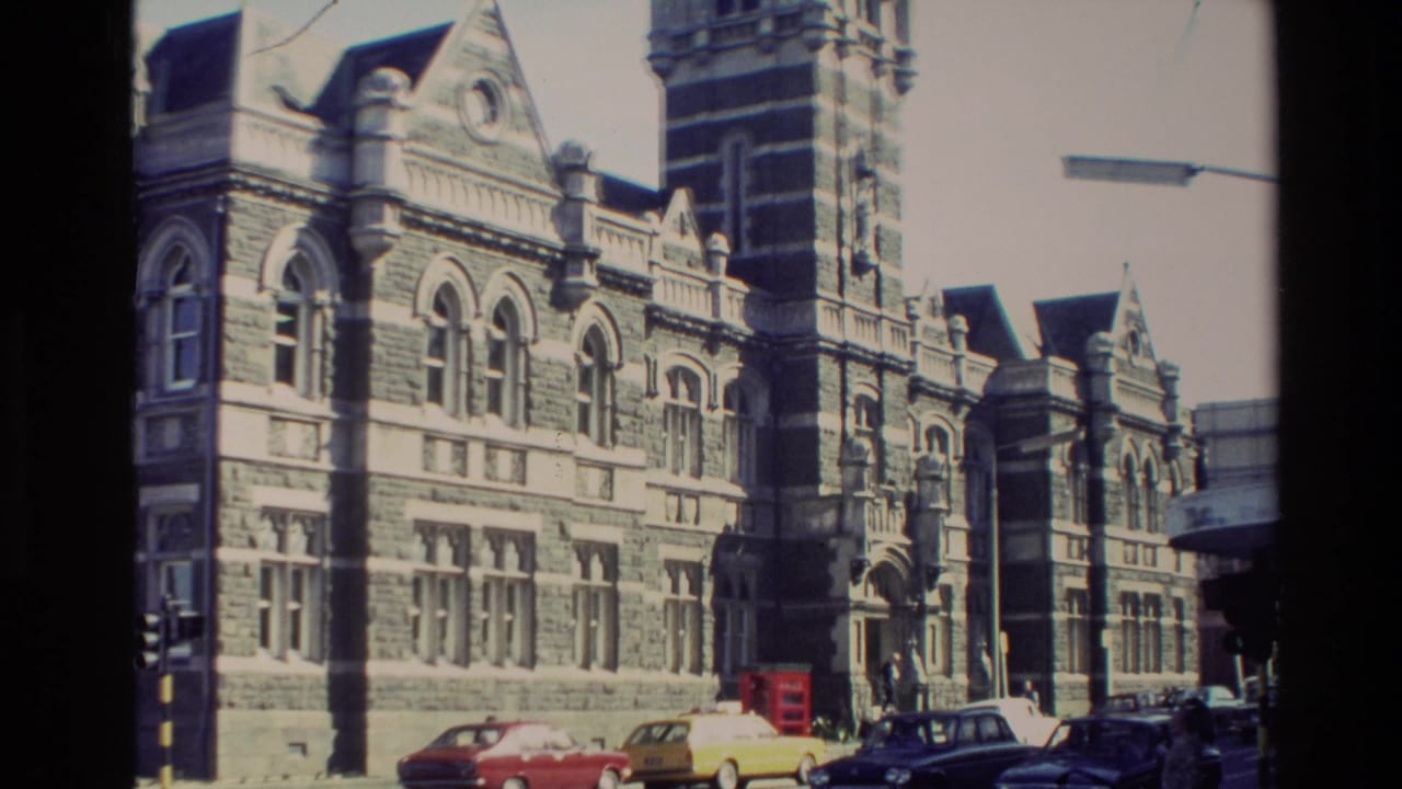 1982 New Zealand 8mm frame showing a large stone cathedral or church exterior with arched windows, tower, parked cars, and street lighting.