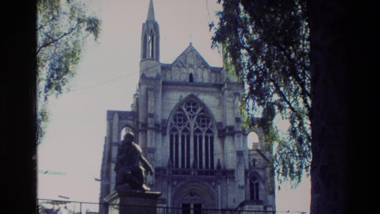 1982 New Zealand 8mm frame showing a Gothic-style church facade, arched window, spire, trees, and a foreground statue.