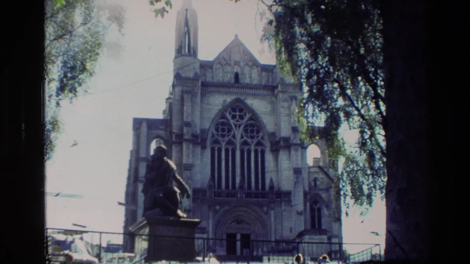 1982 New Zealand 8mm view of a stone church exterior with tracery window, spire, statue, and leafy framing.