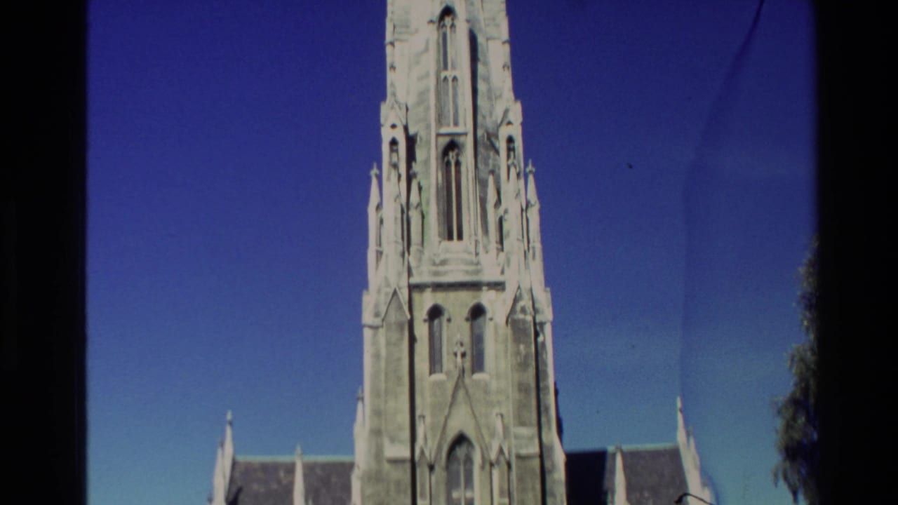 1982 New Zealand 8mm frame showing a pale Gothic-style church tower and roofline against a saturated blue sky.