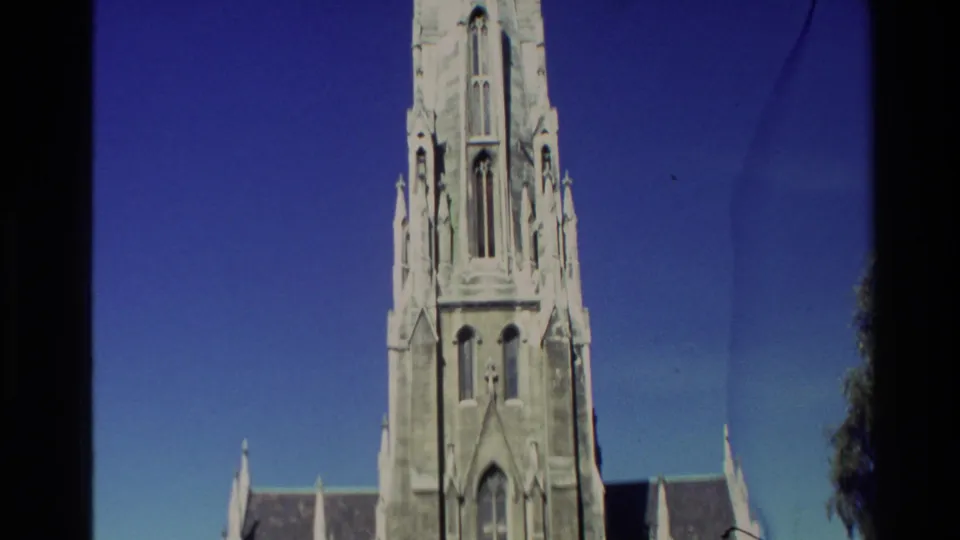 1982 New Zealand 8mm frame showing a pale Gothic-style church tower and roofline against a saturated blue sky.