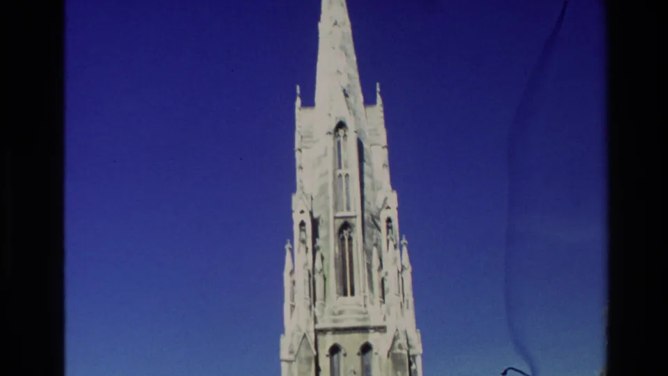1982 New Zealand home-movie frame with the upper church steeple centered against a clear blue sky and visible film edges.