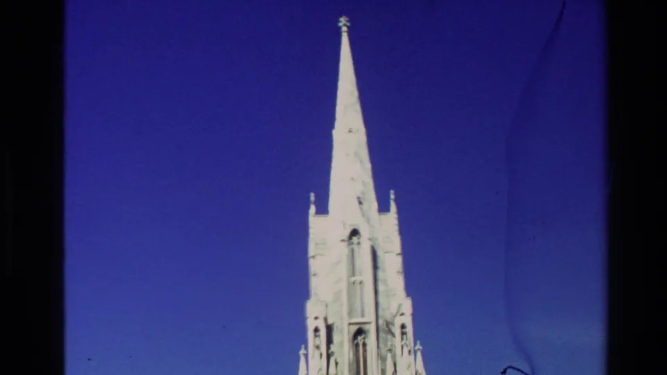 1982 New Zealand 8mm frame emphasizing a tall pointed church spire from a low visitor-shot angle.