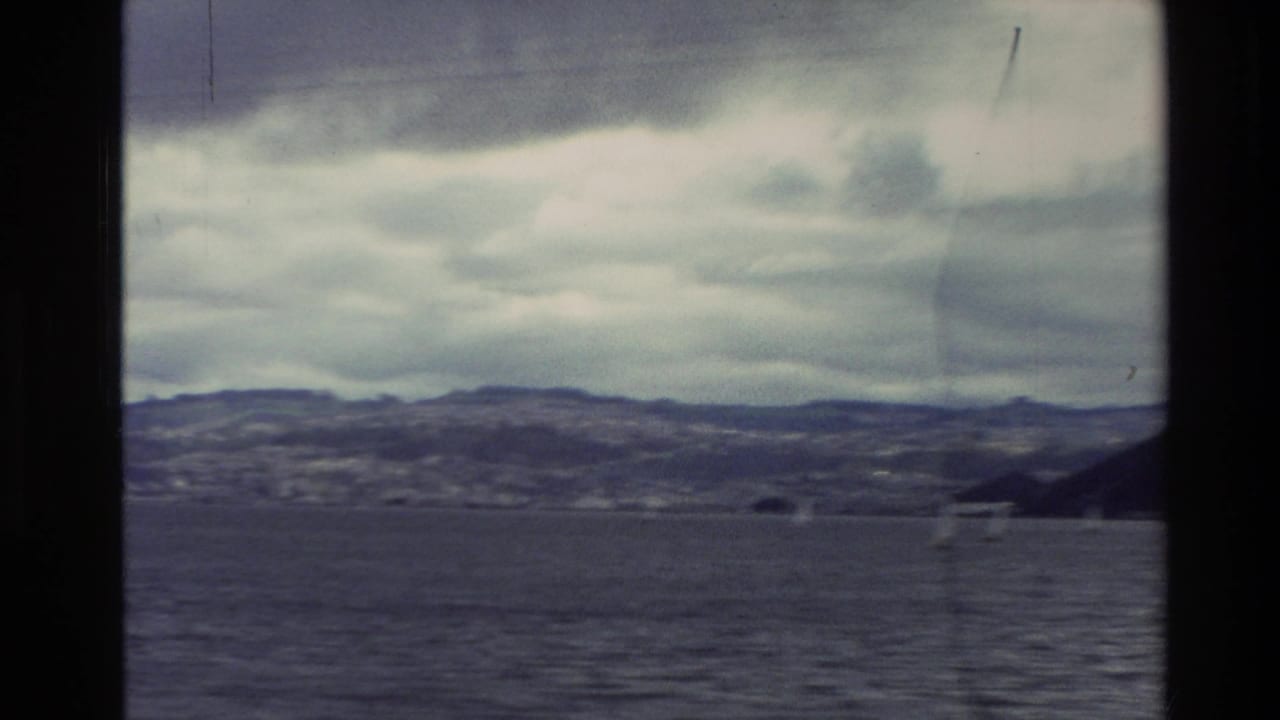 1982 New Zealand 8mm view across a cloudy bay toward low coastal hills, seen through dark frame borders.