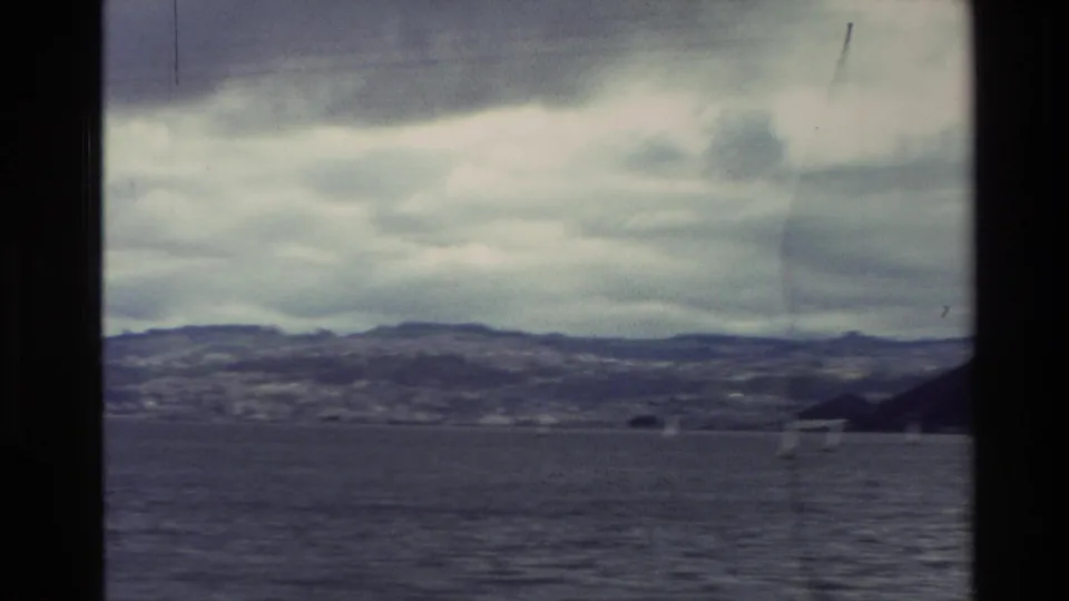 1982 New Zealand 8mm view across a cloudy bay toward low coastal hills, seen through dark frame borders.