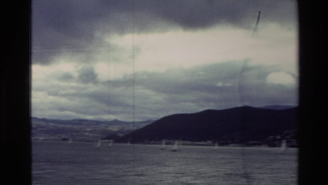 Sailboats on a bay with dark hills and heavy clouds in the distance.