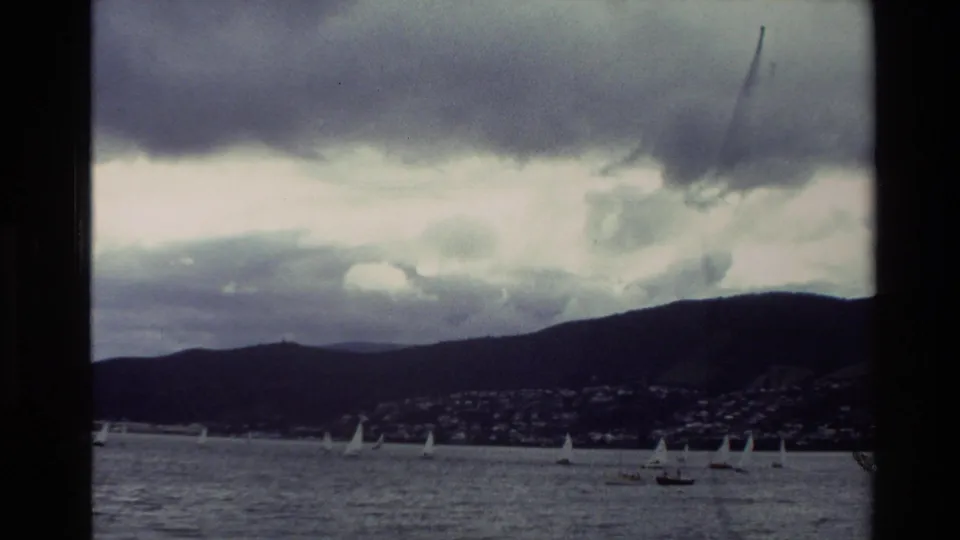 The closing frame shows sailboats scattered across a cloudy New Zealand bay, with a distant town and hills on the shore.