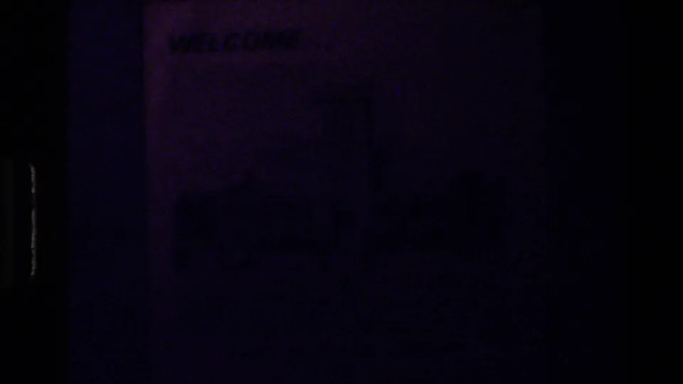 Underexposed home-movie frame with faint printed text and heavy blue-purple color shift, likely part of the guidebook-cover sequence.