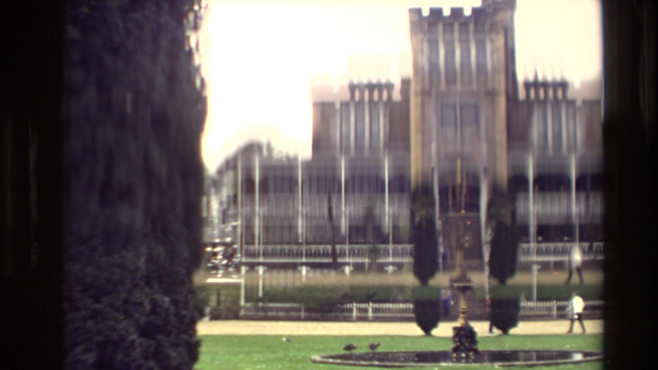 1982 New Zealand 8mm frame showing a stone mansion with tower, verandas, tall evergreens, lawn, and a circular foreground feature.