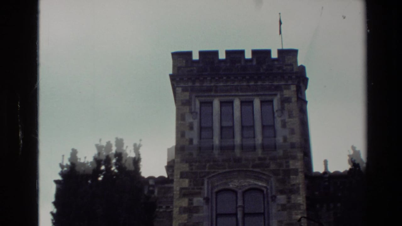 1982 New Zealand home-movie frame showing a stone castle-like building with arched windows, crenellations, trees, and a flagpole.