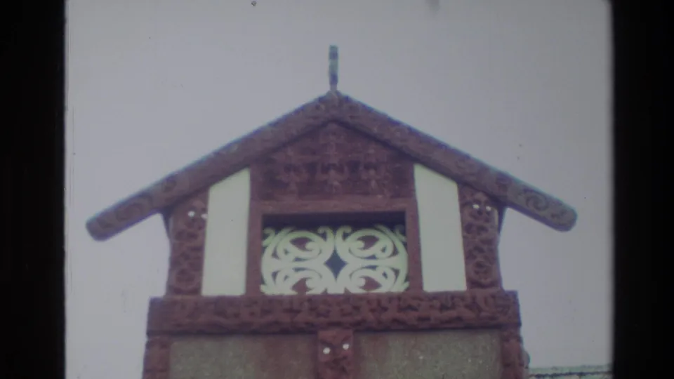 1982 New Zealand frame centered on a carved timber gable and white ornamental panel on a Māori meeting-house style exterior.