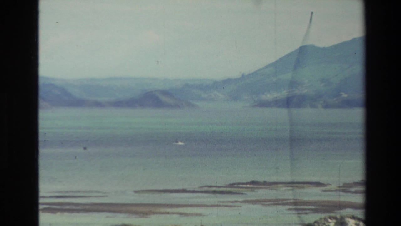 Wide bay with distant hills, low island shapes, cloudy sky, and visible film gate edge.