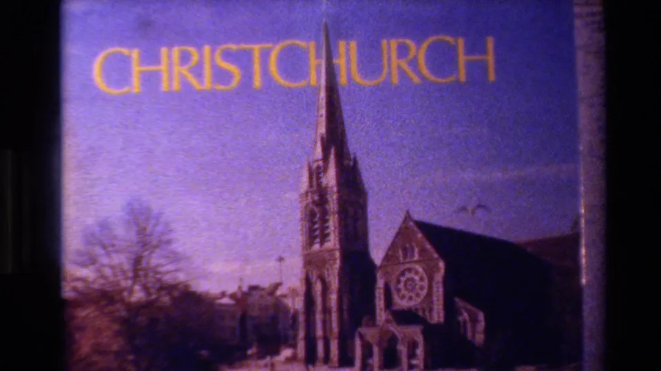 Christchurch title card in 1982 New Zealand travel footage, showing yellow lettering above a purple-tinted view of a church steeple.