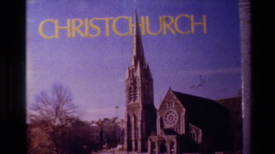 A 1982 New Zealand home-movie frame labels Christchurch above a view of the cathedral facade, spire, bare trees, and dark film border.