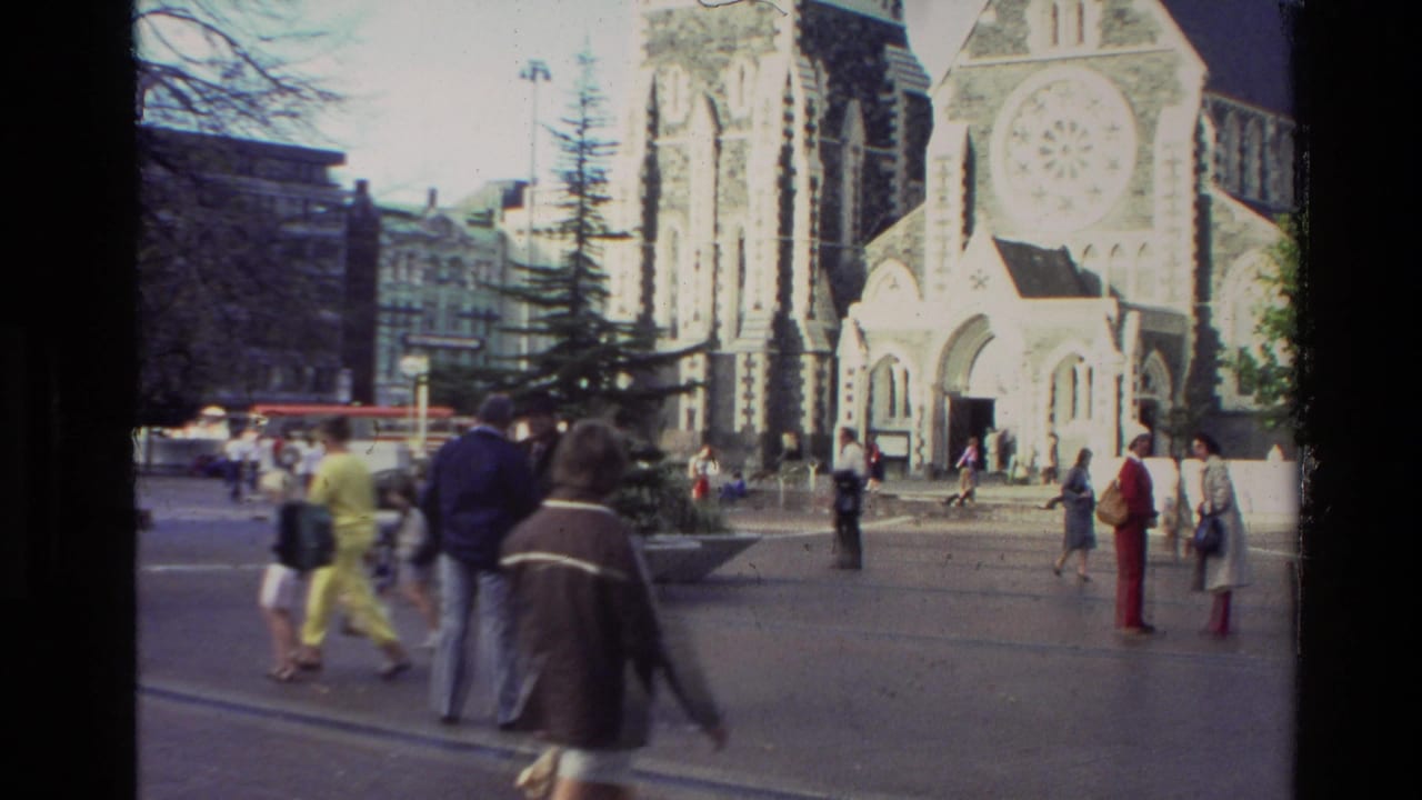 1982 New Zealand home-movie frame showing pedestrians near a Gothic Revival church with a rose window and arched entrance.