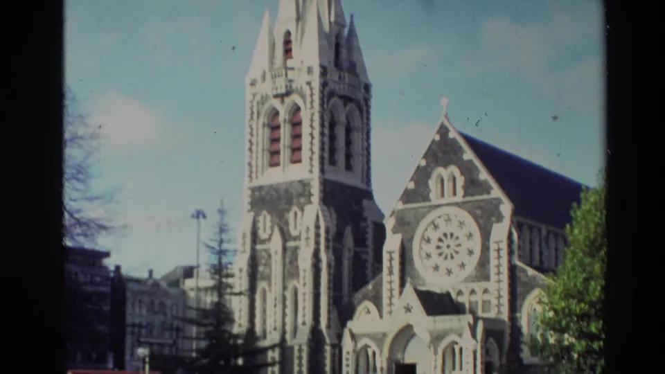A closer upward view shows the church tower, rose window, steep roof, tree line, and surrounding plaza in New Zealand.