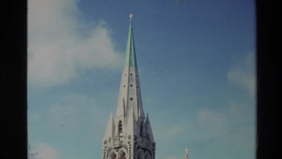 1982 New Zealand 8mm frame with the cathedral spire centered against sky, with part of the tower and roof visible below.
