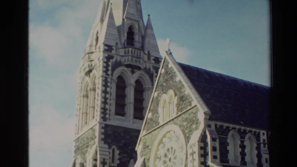 1982 New Zealand 8mm frame of a Gothic-style church exterior with tower, gable and pale trim around arched openings.