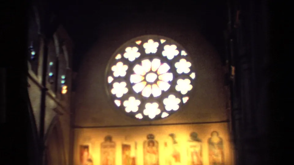 Bright circular stained-glass window and religious imagery inside a New Zealand church, captured on warm 8mm film in 1982.