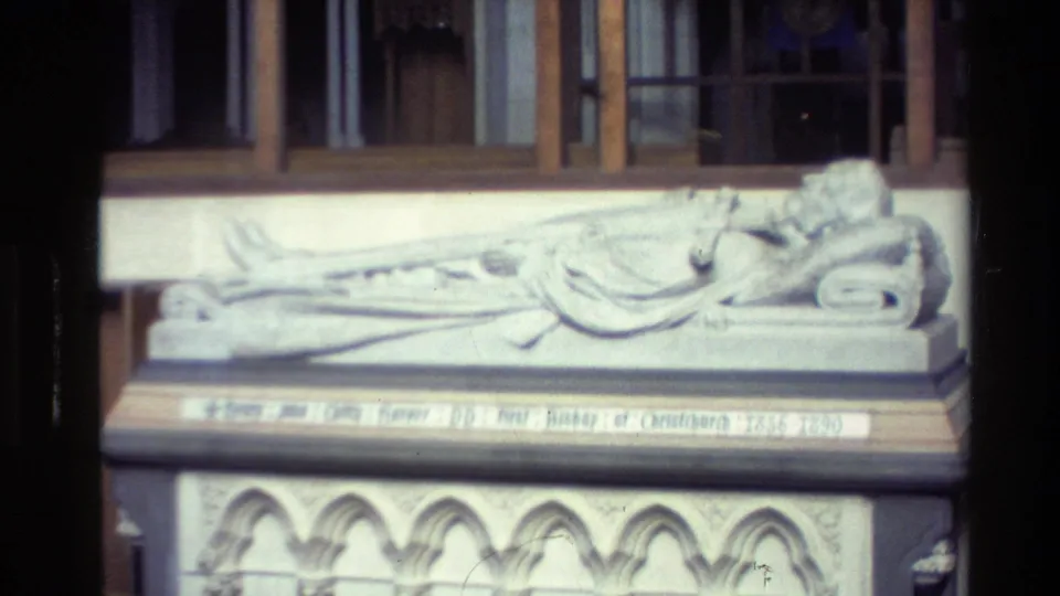 Stone reclining effigy or memorial figure inside a New Zealand church, with inscription band and arched base detail visible in 1982 8mm footage.