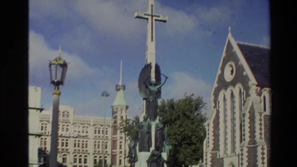 1982 New Zealand 8mm frame of a memorial cross with figures, a church facade, lamp post, and surrounding historic streetscape.