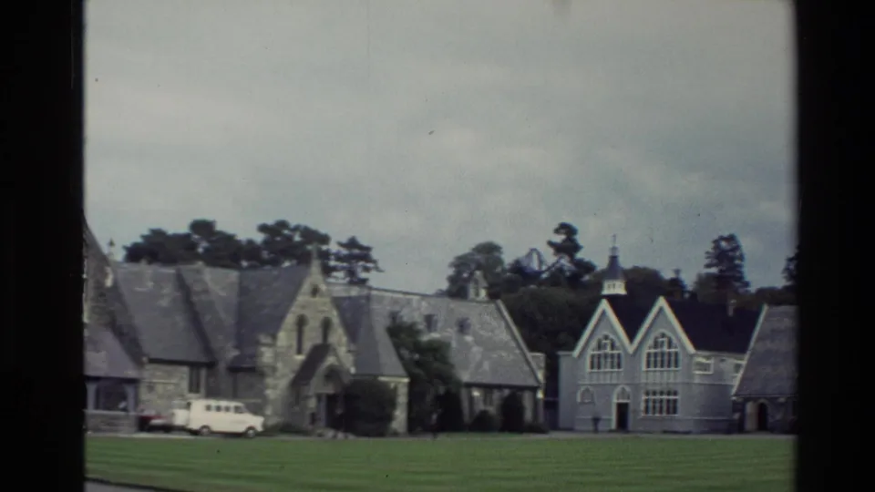 1982 New Zealand campus view showing Christ's College stone buildings, a green lawn, trees, and a parked white van.