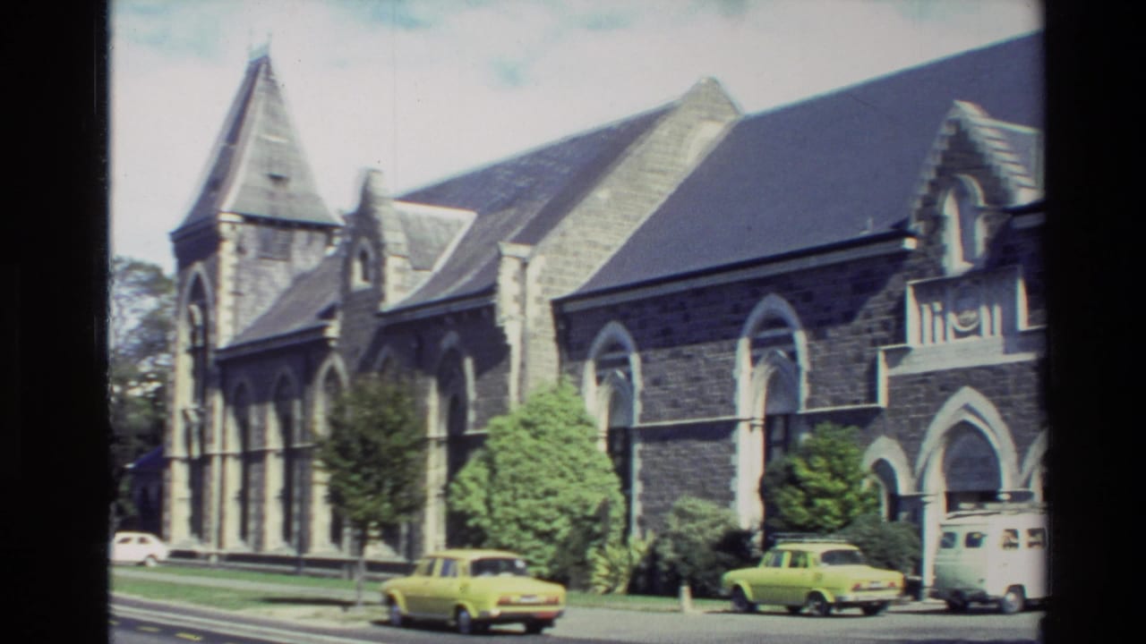 Stone church beside a street with cars and a white van in view.