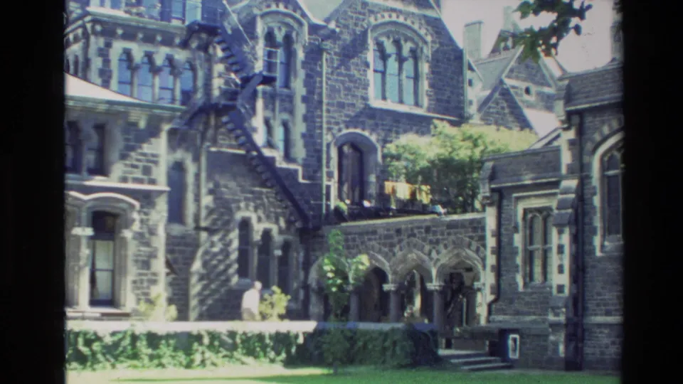 1982 New Zealand 8mm frame with an elderly priest-like figure walking past arched stone openings and a church courtyard wall.