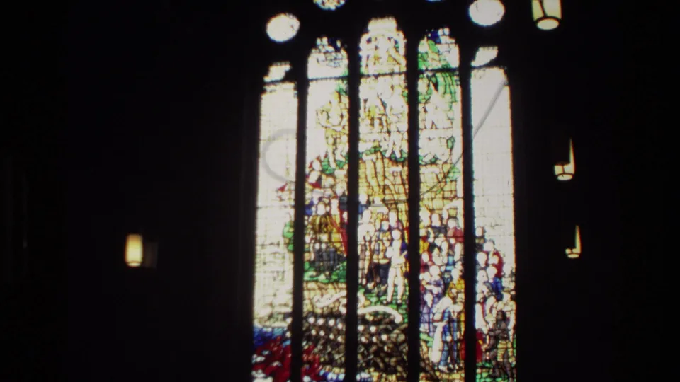 1982 New Zealand 8mm frame showing a tall stained glass church window, dark interior walls, and small hanging lights.