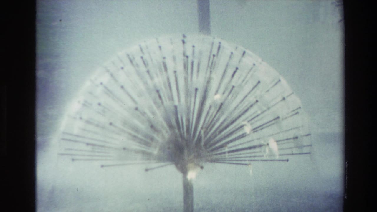 Soft 8mm frame from 1982 New Zealand showing a close view of a spiky spherical fountain spraying water into a misty pond area.