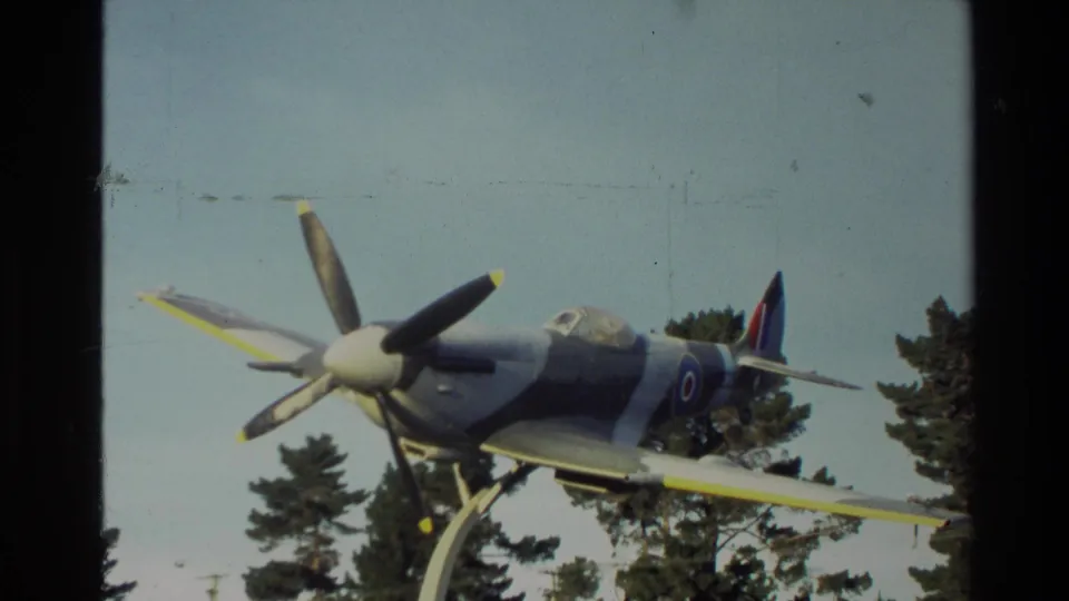 1982 New Zealand home-movie frame showing a propeller aircraft display from a low visitor angle, with trees behind it.