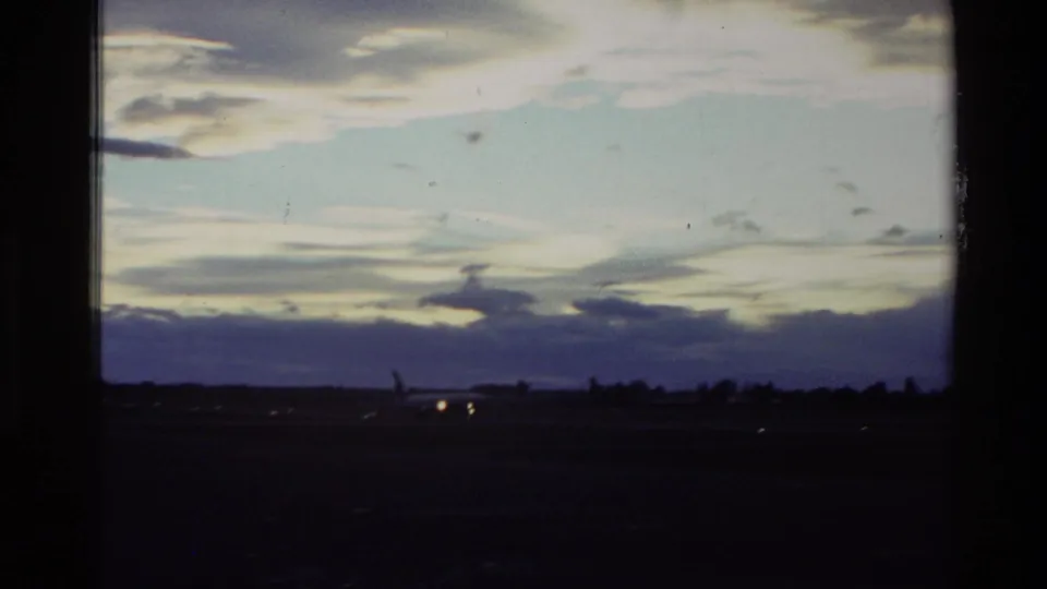 Final 1982 New Zealand 8mm frame shifts to a dark airfield horizon at dusk with small runway lights visible.