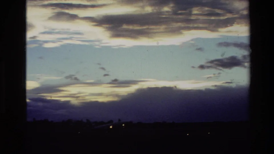 1982 New Zealand 8mm frame with a commercial airplane shape low on the runway beneath layered evening clouds.