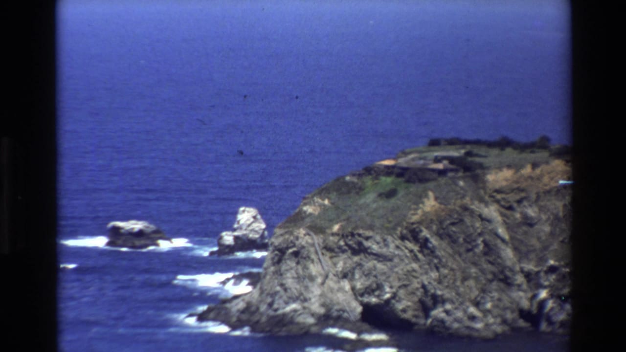 Big Sur coastline in 1980 home-movie footage, with sea stacks, a steep rocky point, white breaking waves, and open Pacific water.