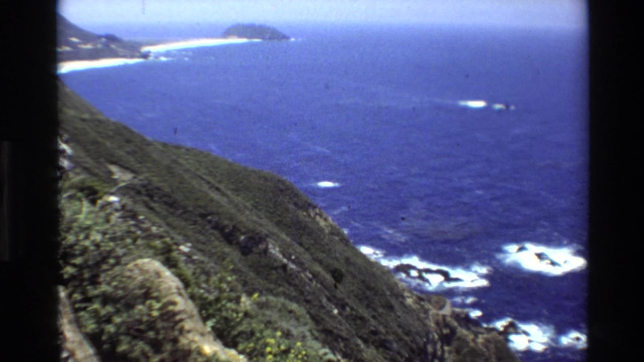Cliffside overlook across blue ocean with white surf and distant shoreline.