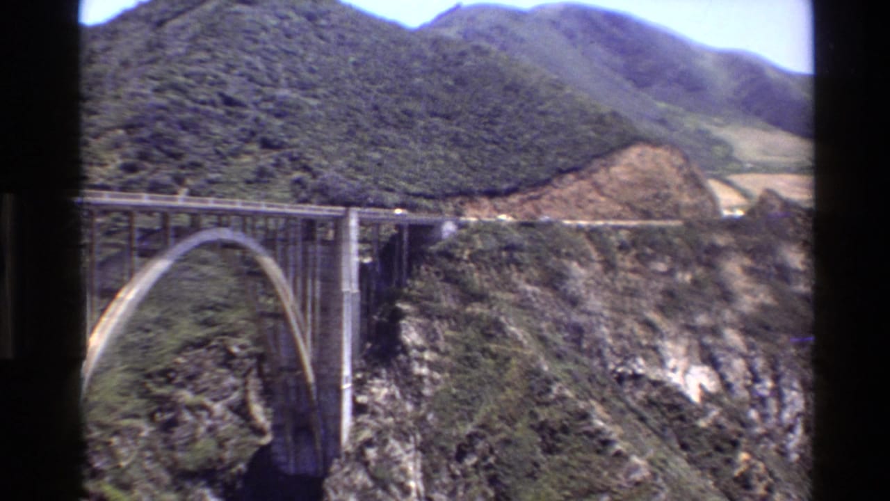 Arch bridge and highway crossing a canyon with cars visible on the road.