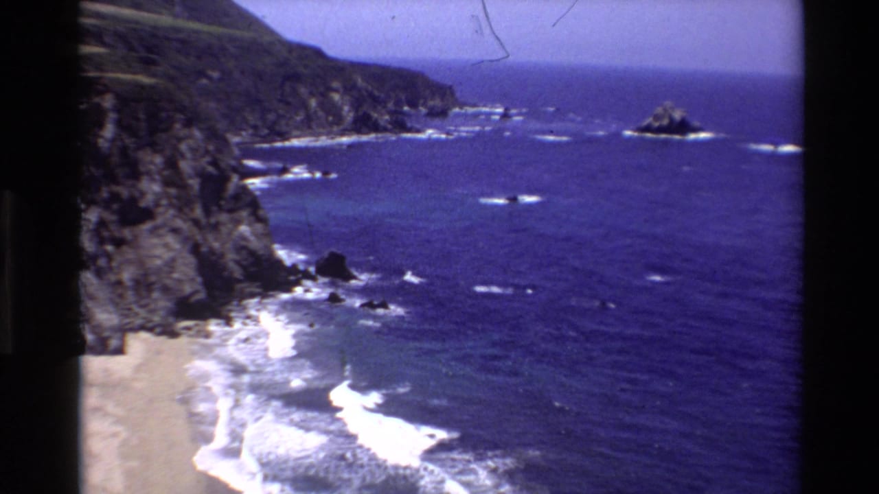 Rocky coastline and blue ocean with surf lines and offshore rocks.