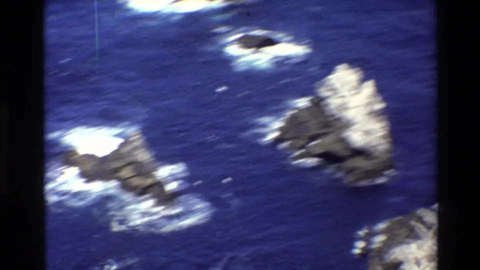 1980 Big Sur 8mm aerial view of offshore rocks in blue water, with motion blur and white surf around the sea stacks.