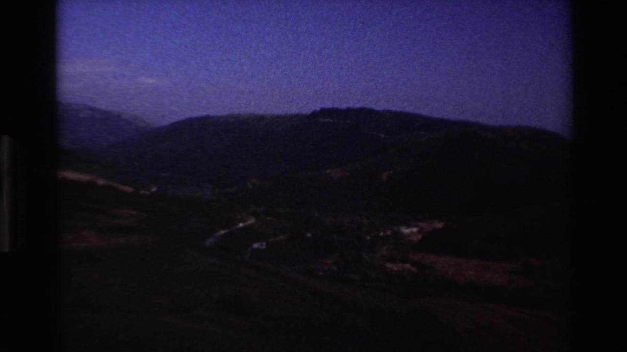 Underexposed 8mm frame of Big Sur hills at the start of a light transition, with dark slopes and a faint sky.