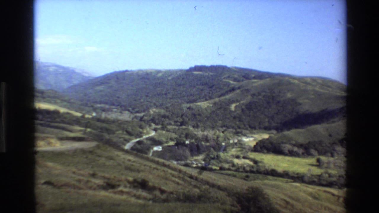 Sunlit green hills with a winding road and blue sky.