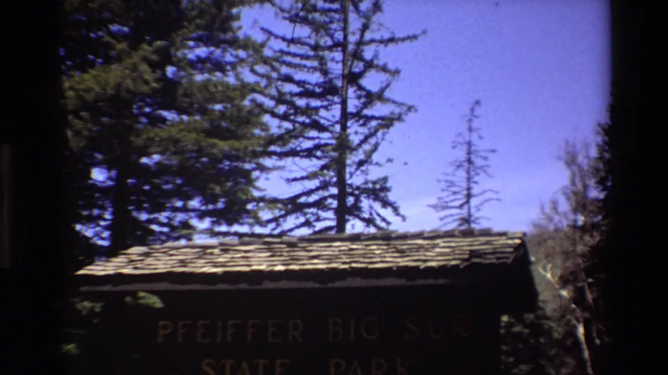 1980 8mm view of the Pfeiffer Big Sur State Park entrance sign partly shaded under tall evergreens.