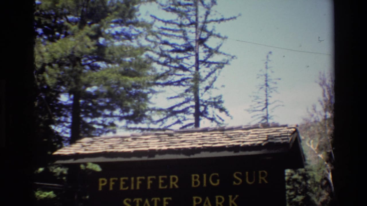 1980 home-movie frame showing the Pfeiffer Big Sur State Park sign, its roofline, and surrounding trees.