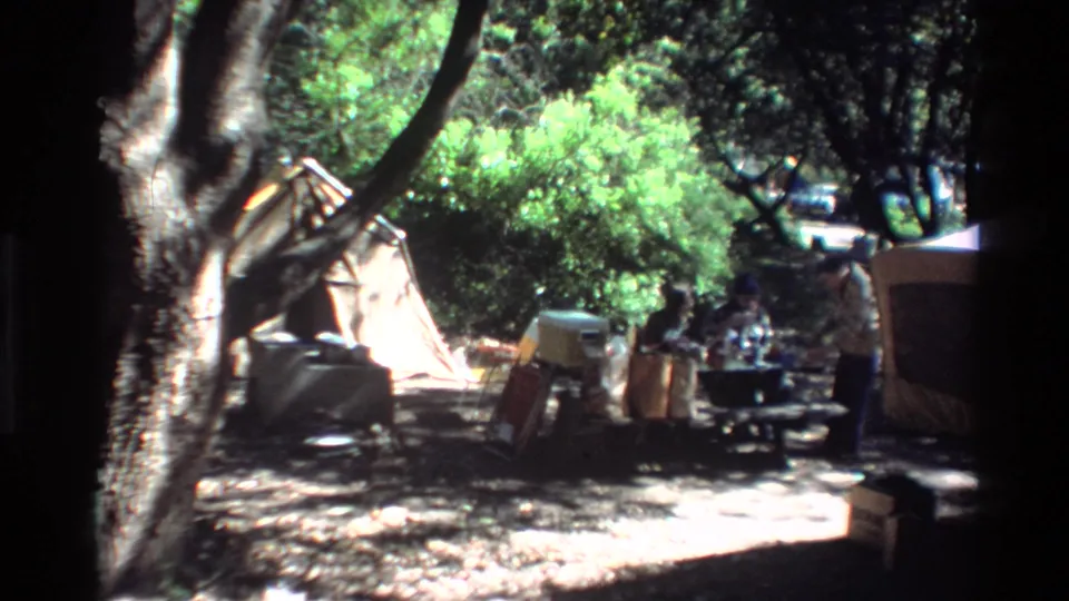 Big Sur campsite around 1980 with dense trees, a canvas tent, folding chairs, coolers, and people near a picnic table.