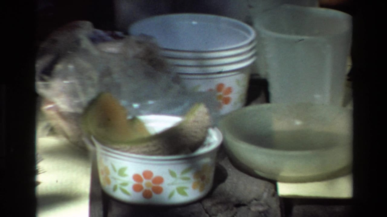 Close view of floral bowls, stacked plates, cups, and melon pieces on a table.